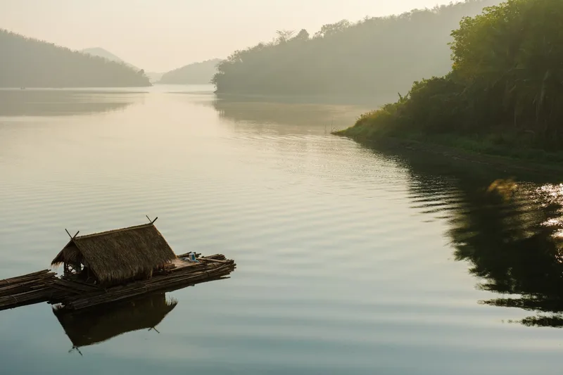 A thatched bamboo raft drifting on a misty river at dawn in Isaan, northeast Thailand