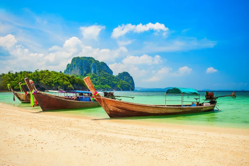 Longtail boats beached on white sand below a limestone island in the Gulf of Thailand